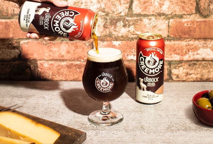A can of Urbock beer is being served in a glass next to another can of Urbock beer, Image