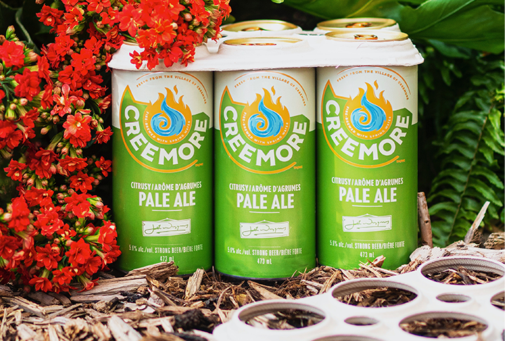 A six pack of 473ml Pale Ale beer cans next to some red flowers